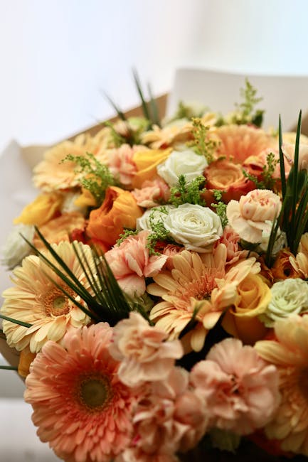 A vibrant floral arrangement featuring a mix of peach, pink, orange, and white flowers, including roses, gerbera daisies, and lisianthus, accented with greenery such as palm leaves and small filler fo